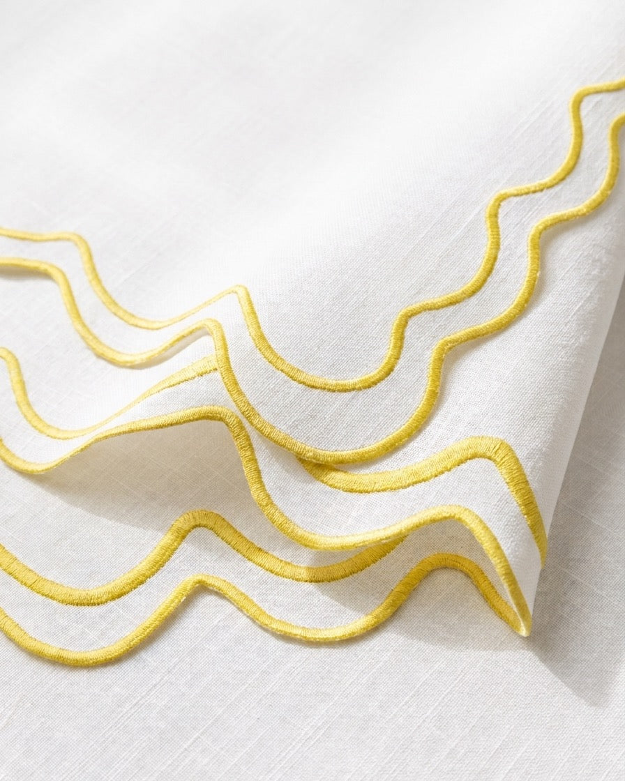 A close-up of a white napkin featuring elegant wavy yellow embroidered borders