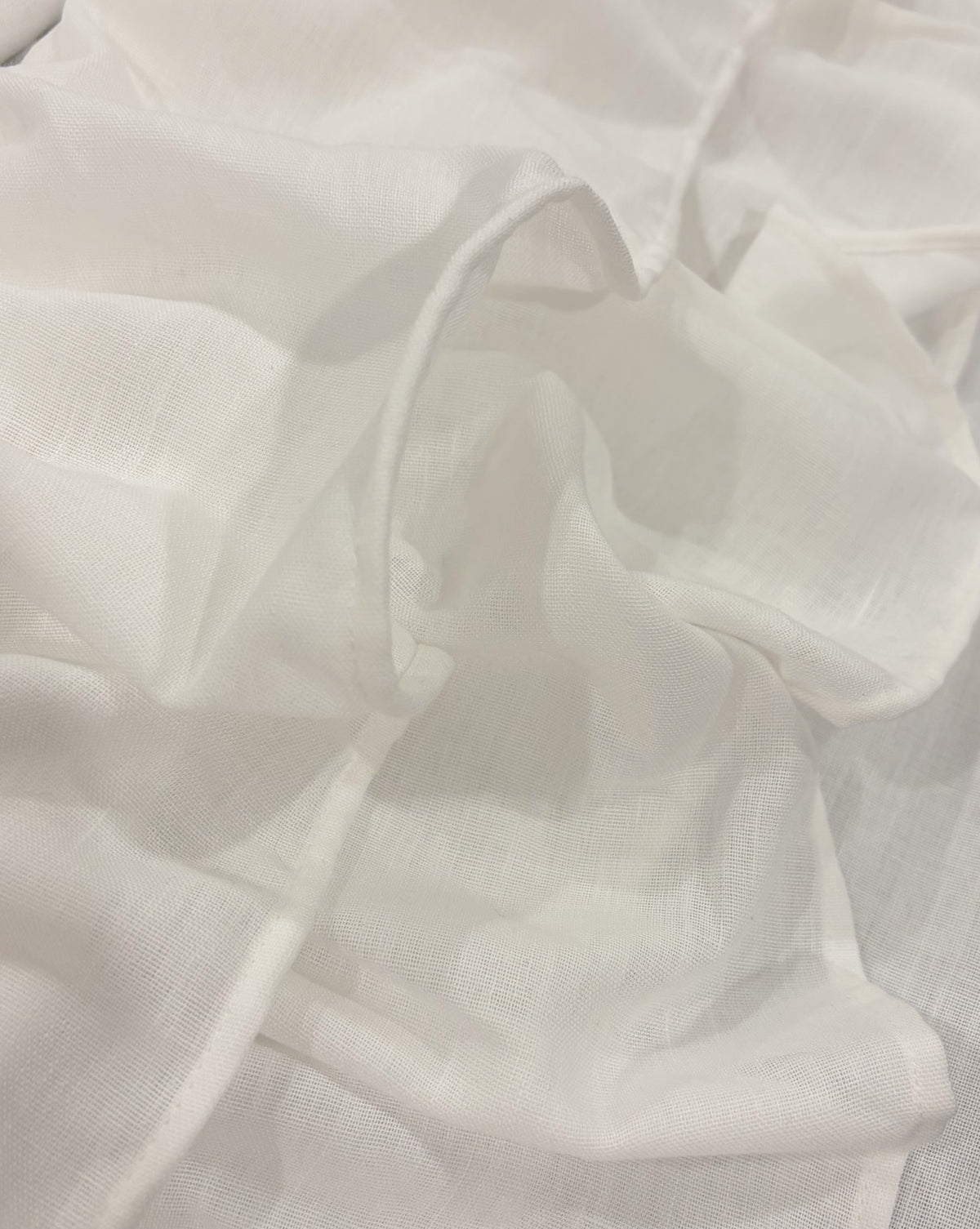A close-up of draped white fabric with a soft, slightly sheer texture and gentle folds.