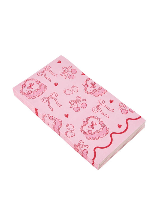 A stack of pink paper napkins featuring a repeating pattern of red bows, cherries, strawberries, and hearts, shown on a plain white background.